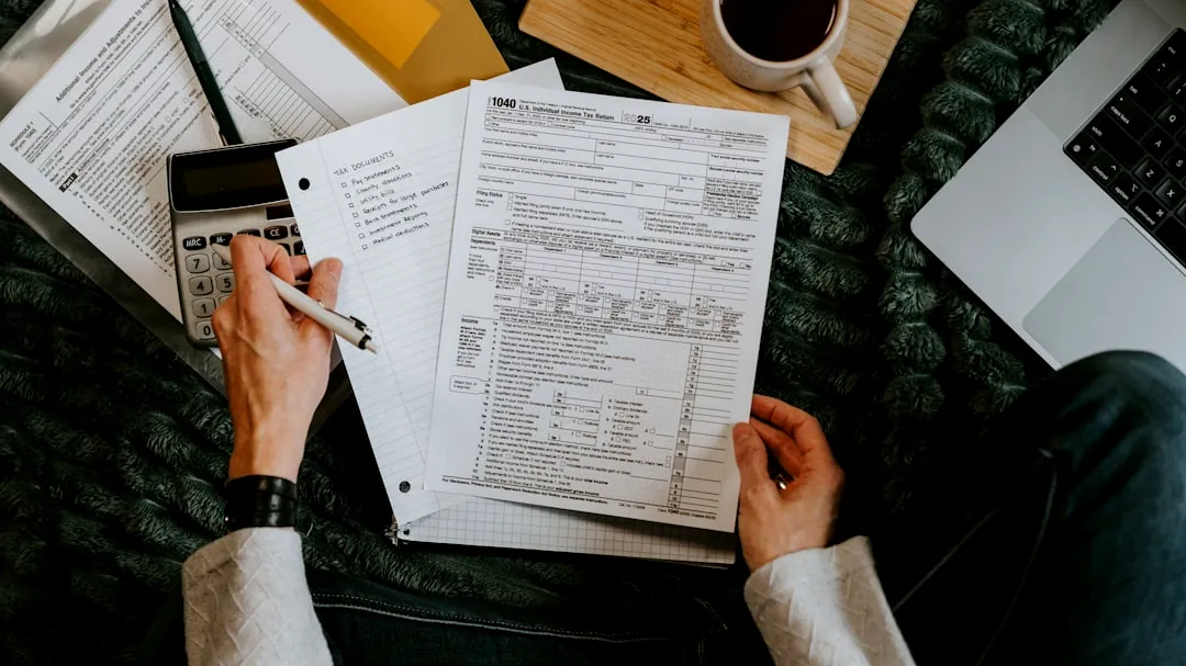 Person reviewing documents with calculator and laptop.