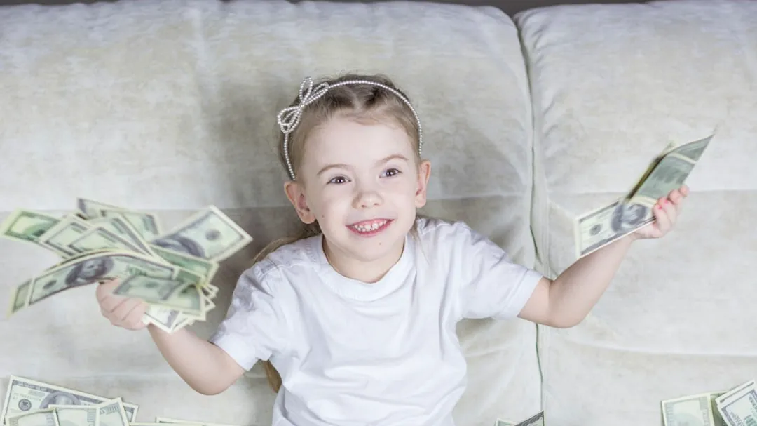 a little girl sitting on a couch holding money