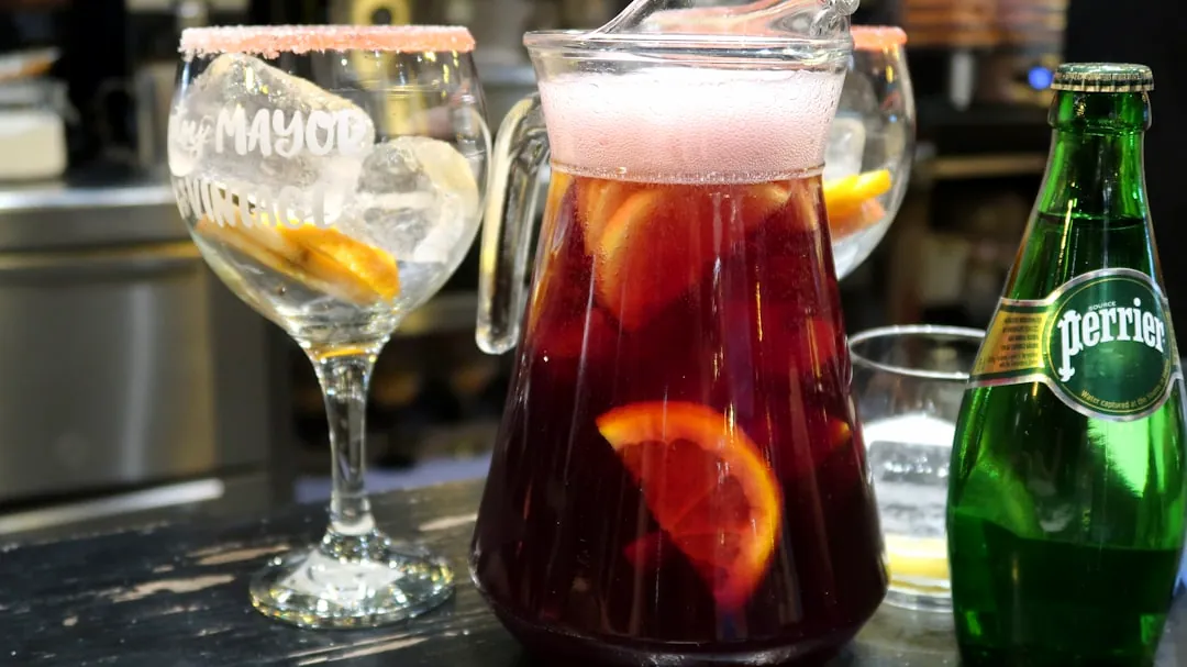 Refreshing sangria pitcher, glass, and perrier bottle on a bar.
